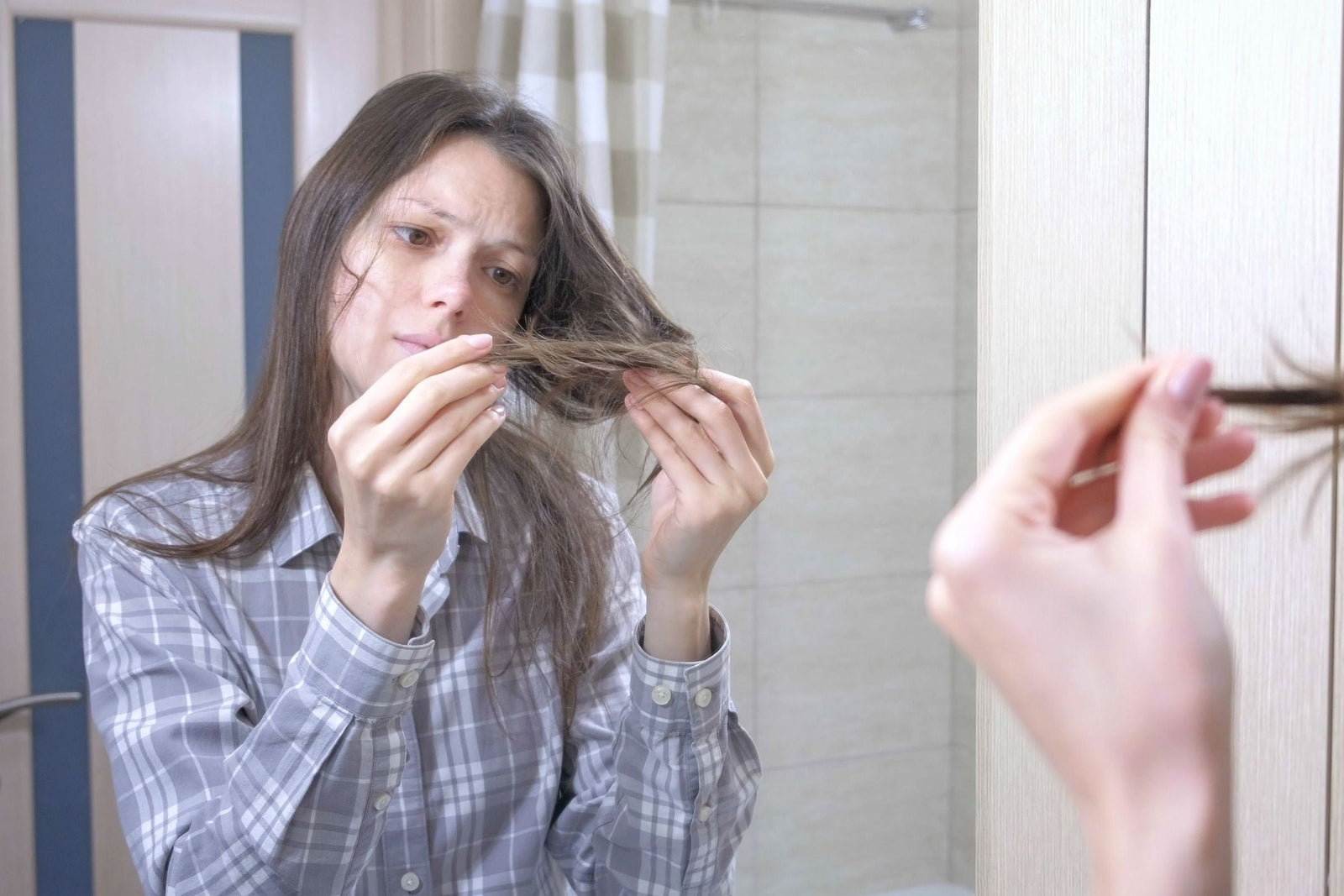 Woman looking at her hair in mirror concerned that her hair is looking dry and damaged.