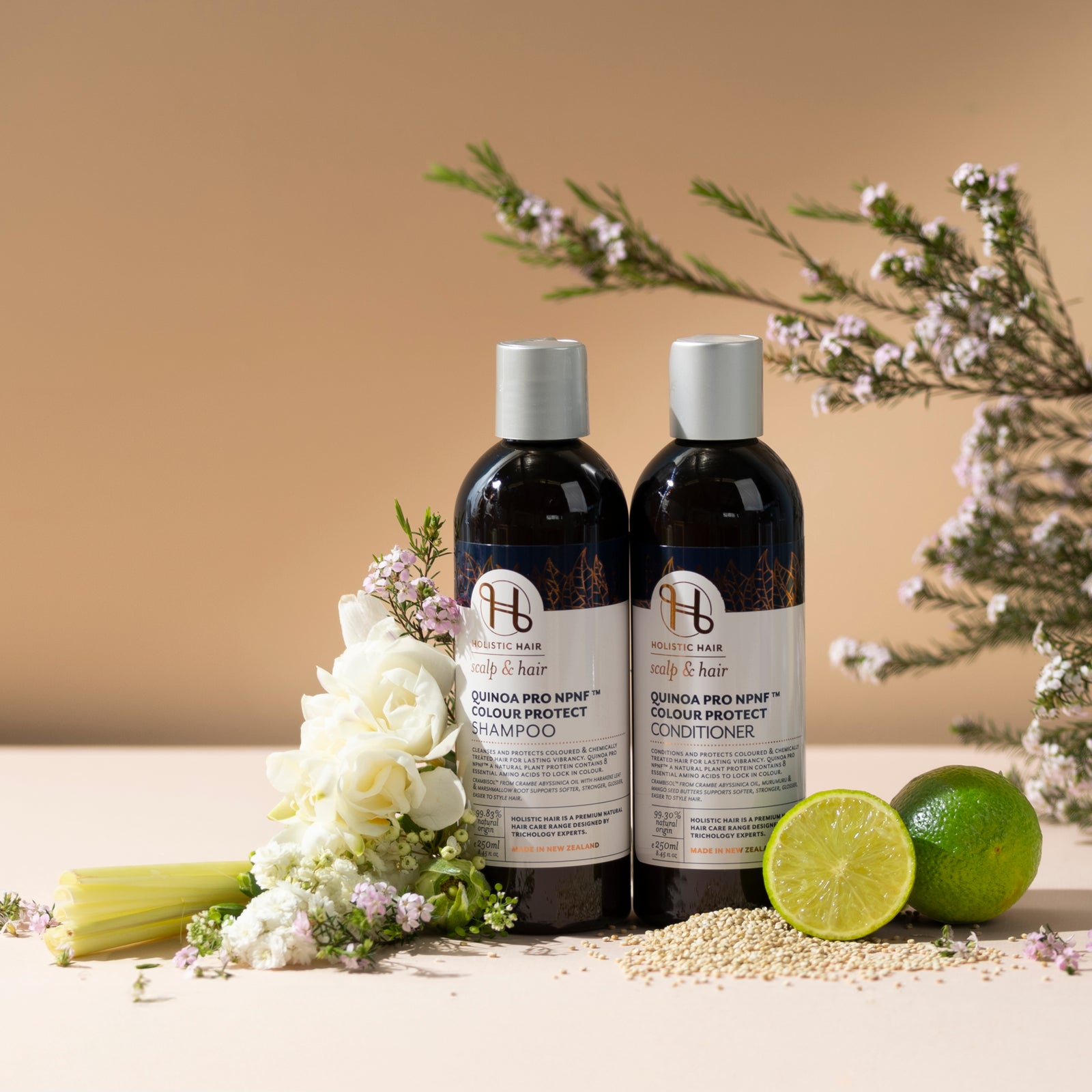 Holistic Hair Quinoa shampoo & conditioner products with flowers and a lime on a beige background