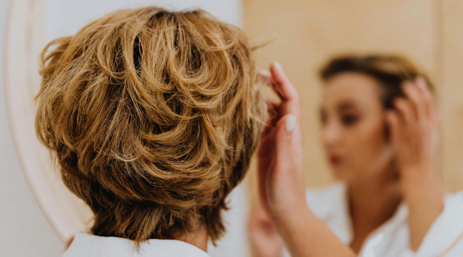 Women looking into mirror admiring her beautiful healthy hair after using Holistic Hair products.